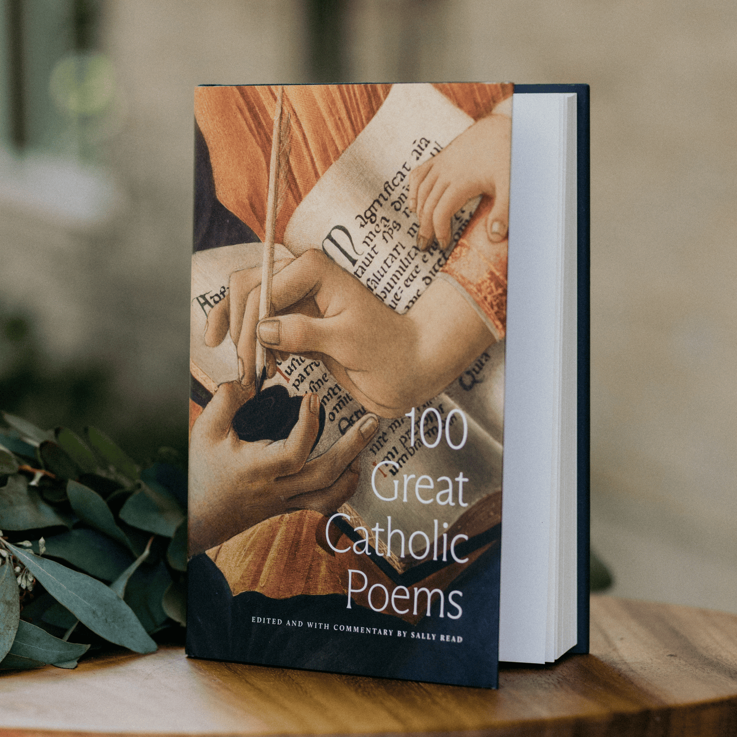 Book titled "100 Great Catholic Poems" featuring an artistic cover of hands writing on parchment, edited with commentary by Sally Read, book of Catholic poetry, Word on Fire, hardcover 9781685780746