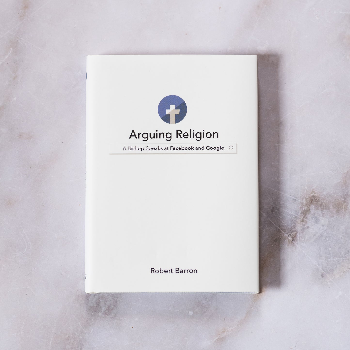 Book titled "Arguing Religion: A Bishop Speaks at Facebook and Google" by Robert Barron, with a simple white cover featuring a cross icon inside a blue circle, displayed on a marble surface, by Bishop Robert Barron, books on religion and culture, hardcover 9781943243372