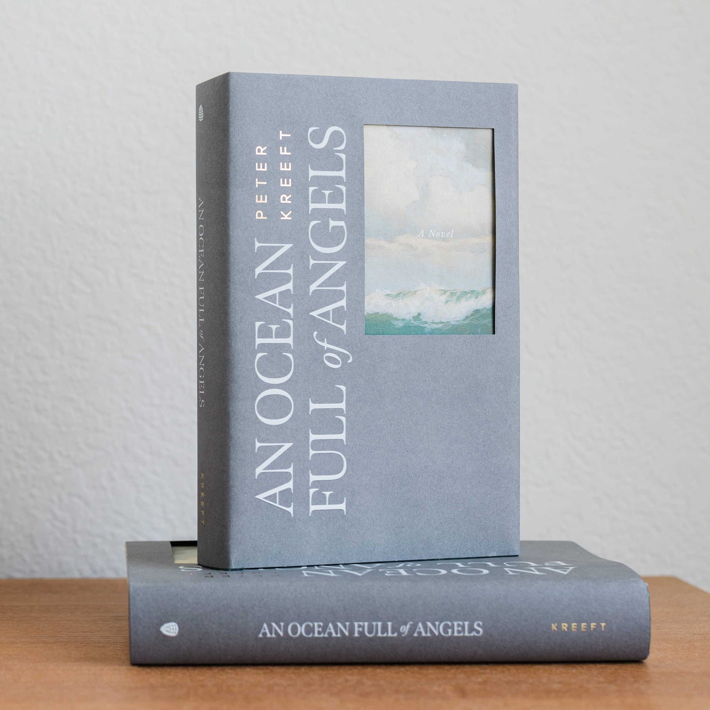 Two copies of the book An Ocean Full of Angels by Peter Kreeft with a blue-gray cover featuring a small painting of ocean waves under a cloudy sky, Catholic fiction novel, Word on Fire Luminor, hardcover 9781685783075