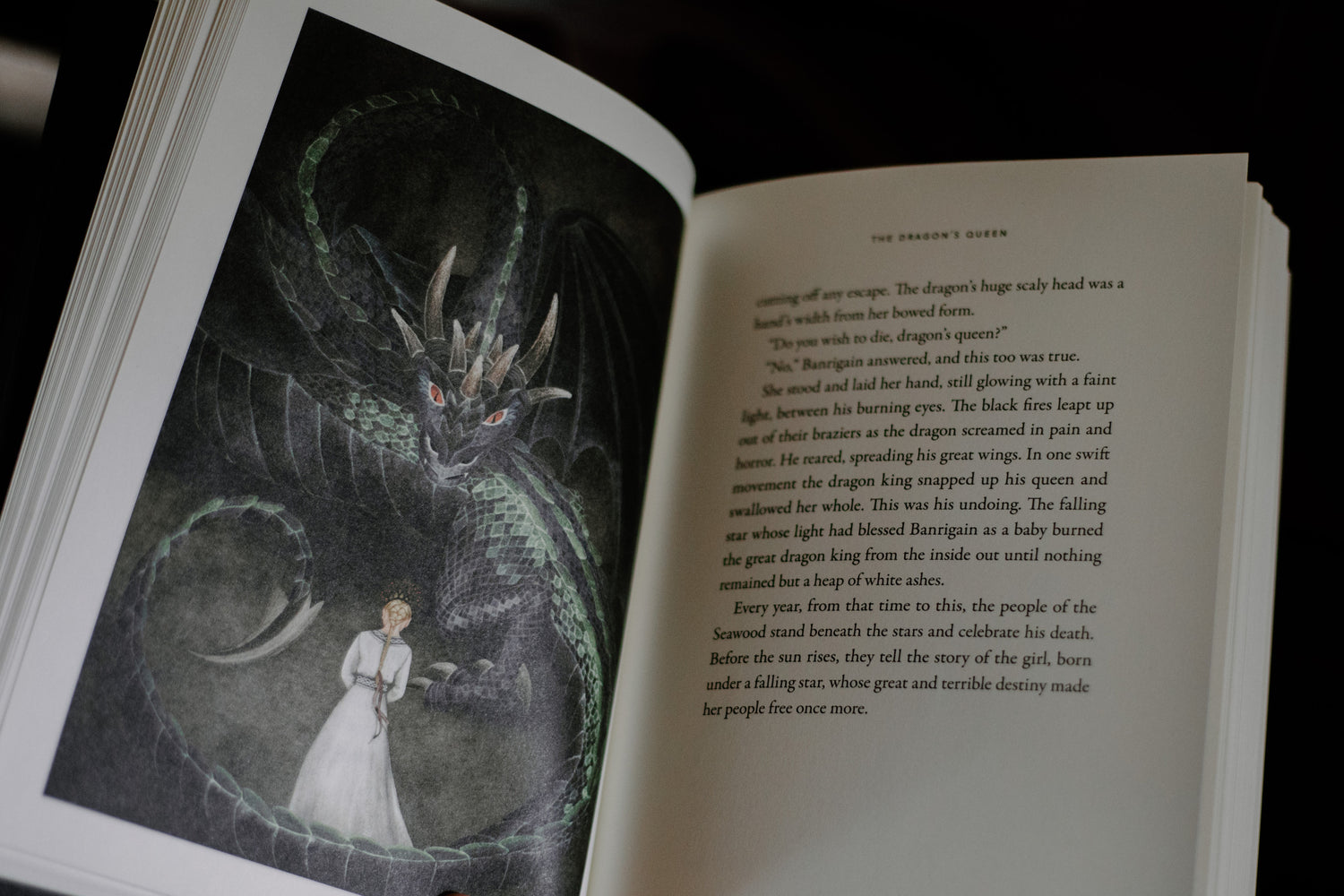 Open book showing a dark illustration of a dragon and a woman in white opposite a page of printed text titled The Dragon's Queen, hardcover, Past Watchful Dragons