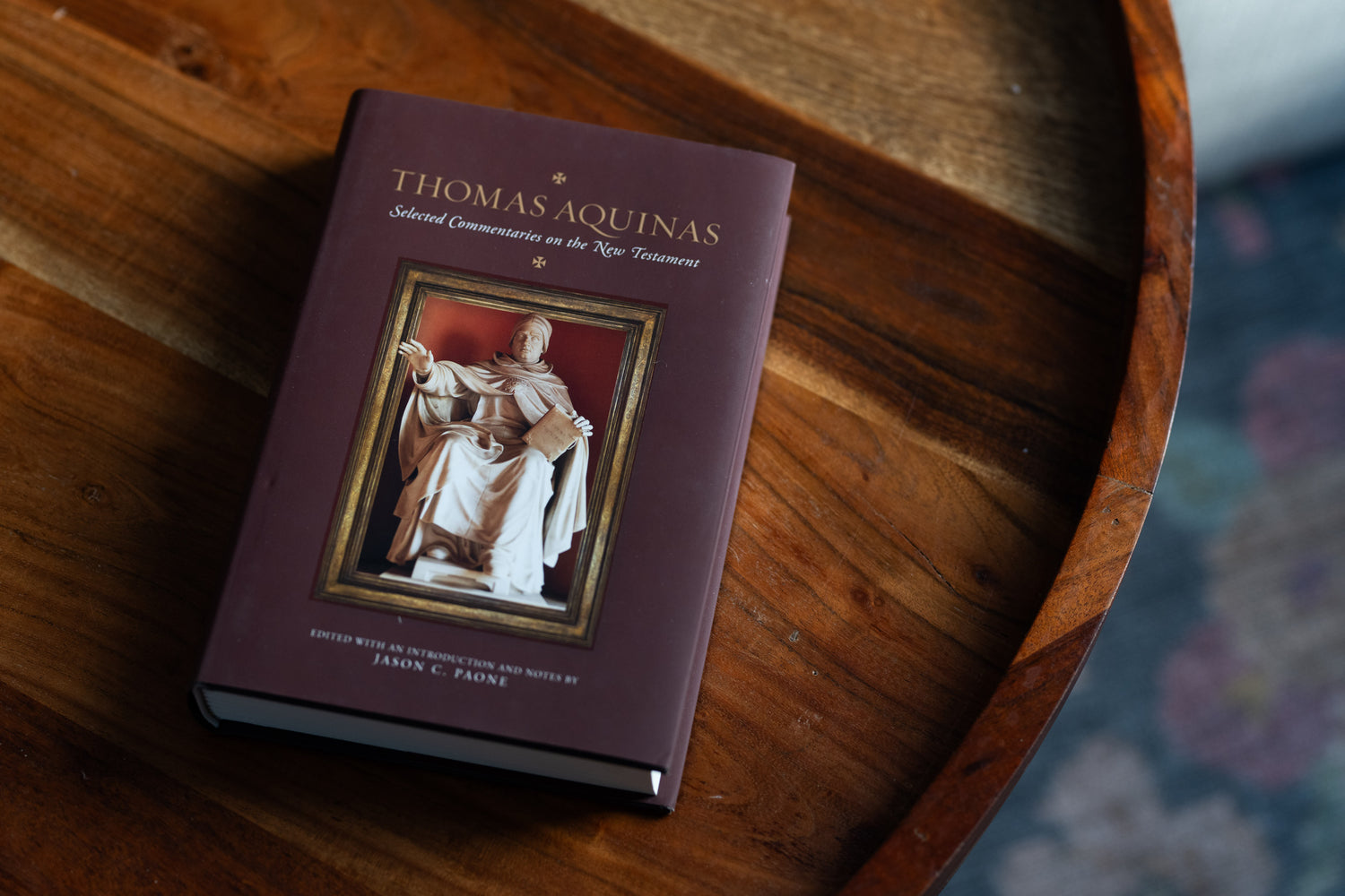 Hardcover book titled Thomas Aquinas Selected Commentaries on the New Testament resting on a wooden circular table
